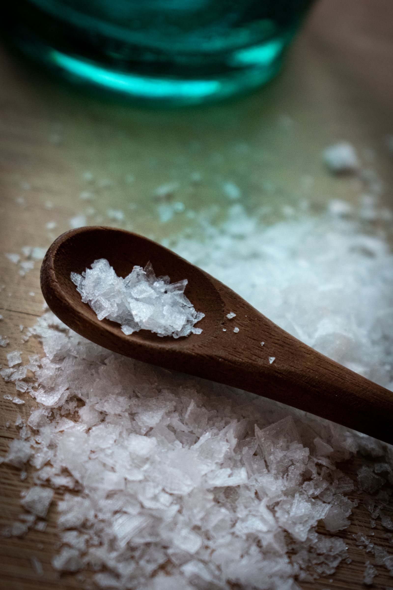 Wooden scoop holding coarse salt crystals beside a jar